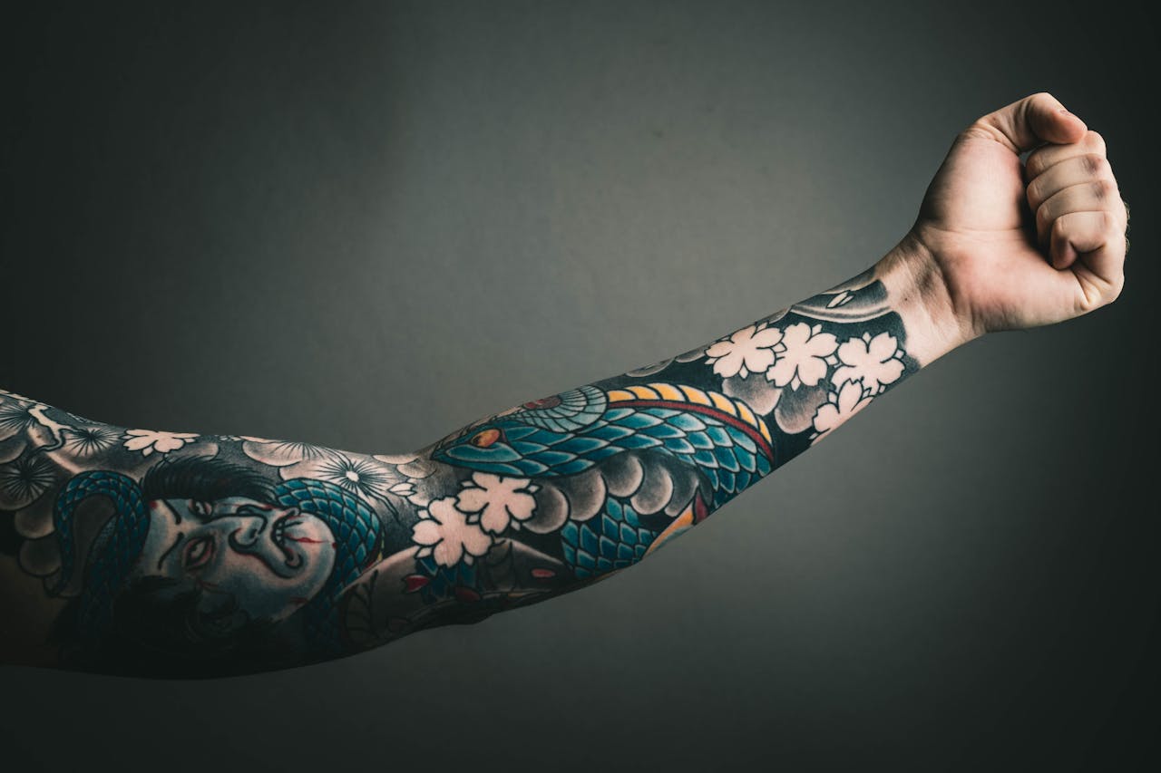 heros-img A close-up of a tattooed arm with a colorful sleeve design, featuring floral and artistic elements.