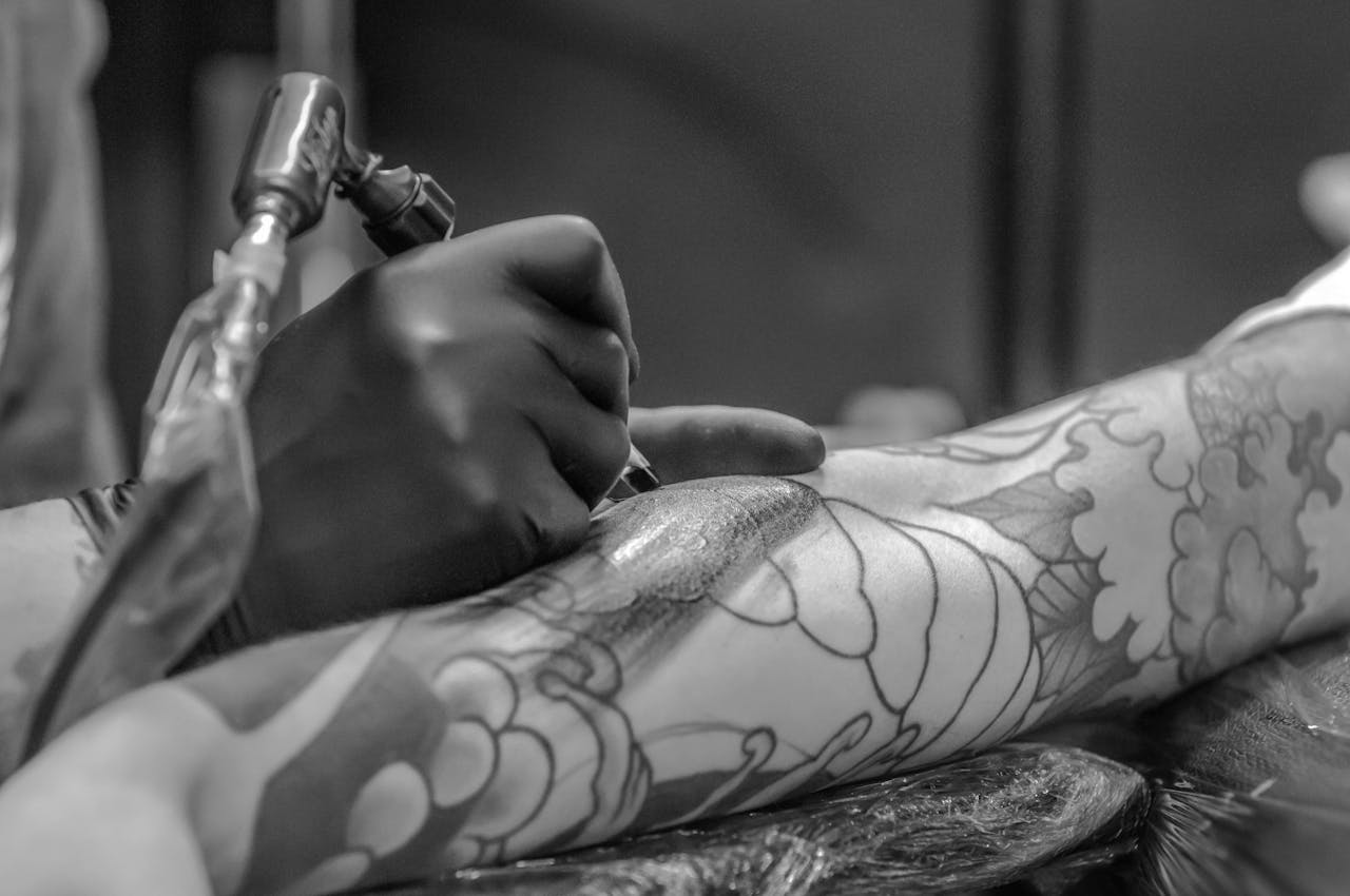 about-us Artistic black and white photo capturing the detailed process of tattooing an arm.